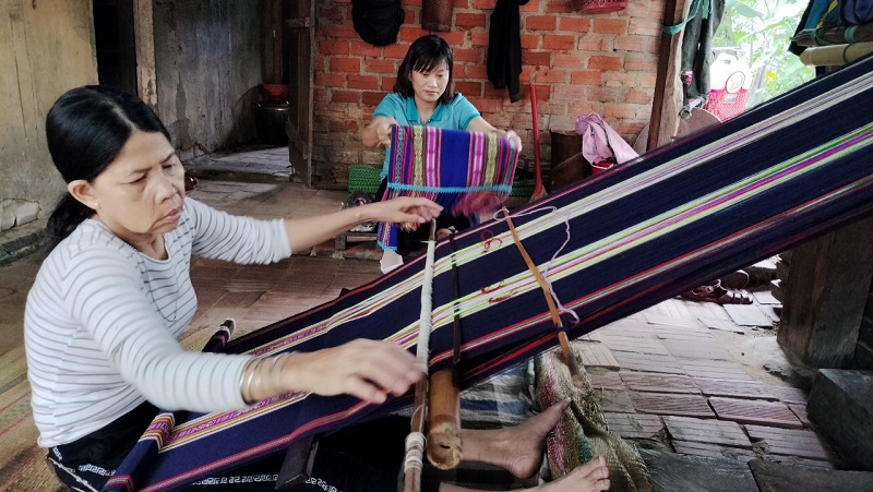 Bà Đinh Thị Nghiêm thành viên mô hình dệt thổ cẩm xã Vĩnh An tranh thủ việc nhà, tiếp tục hoàn thành sản phẩm theo đơn đặt hàng của Hội Phụ nữ